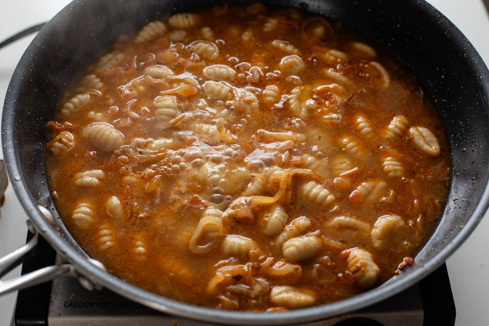 Gnocchi, broth, and shallots in a skillet.