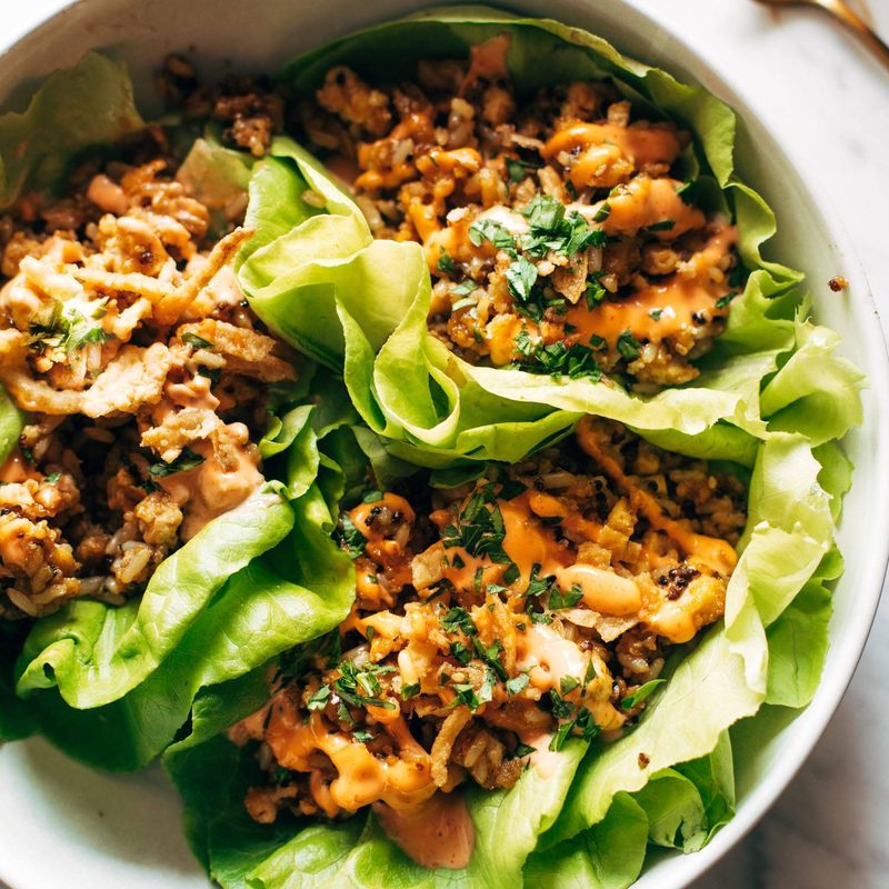 Lettuce wraps on a plate. The wraps are filled with tofu and brown rice and have sauce drizzled on top.