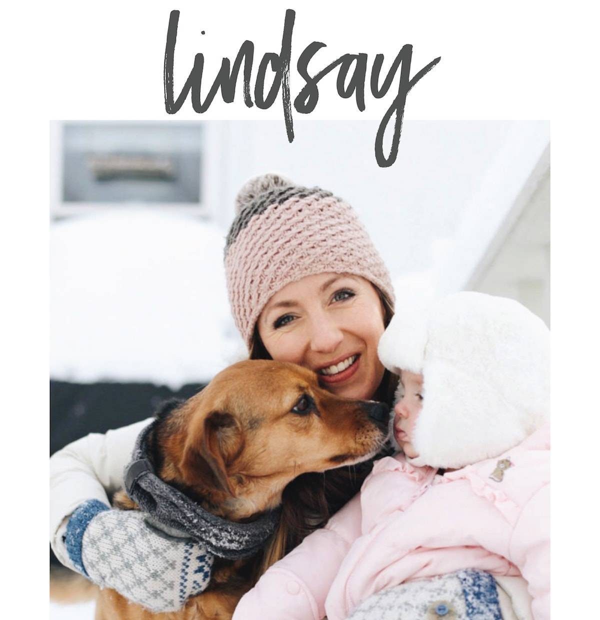 Woman is holding her kid and dog with a broad smile.