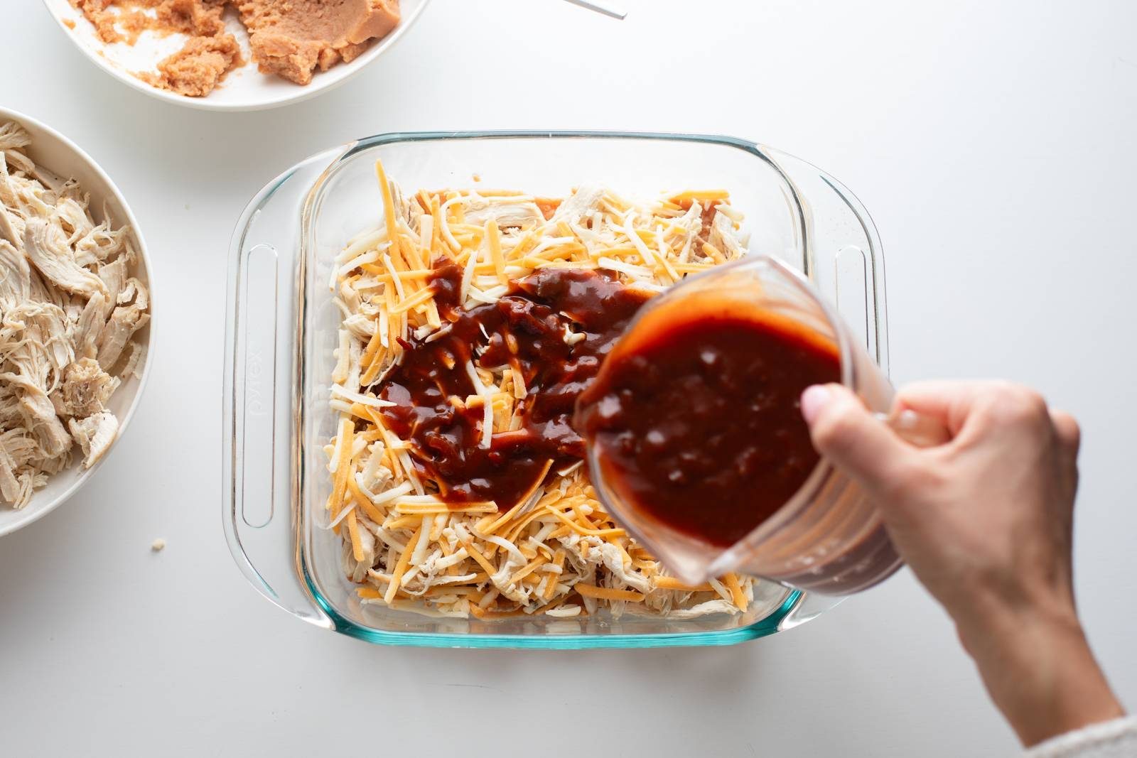 Adding more enchilada sauce to an enchilada casserole.